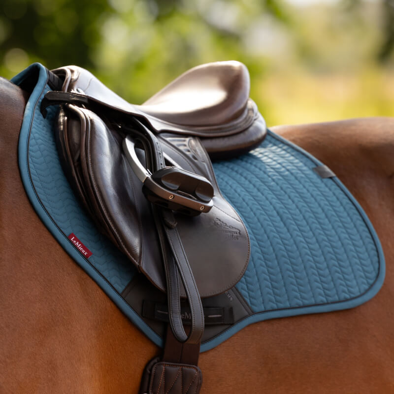Brown saddle and black stirrup on LeMieux Essence Close Contact Square Jungle atop a horse outdoors.