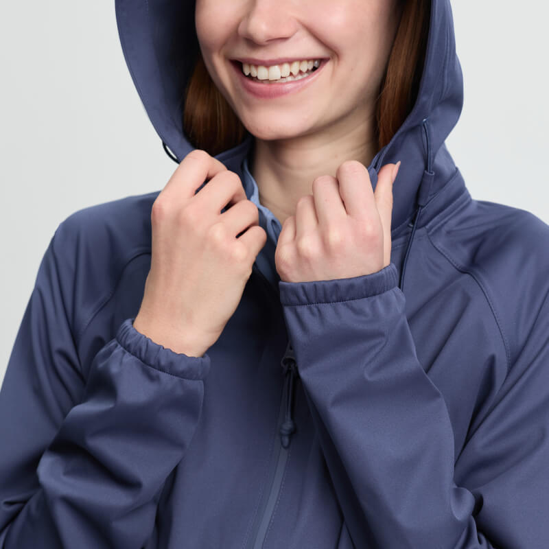Smiling person in LeMieux Perri Half Zip Waterproof Hoodie Shadow, holding the hood with both hands.