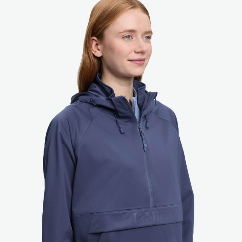 Person with long hair in a blue LeMieux Perri Half Zip Waterproof Hoodie, facing right and smiling.