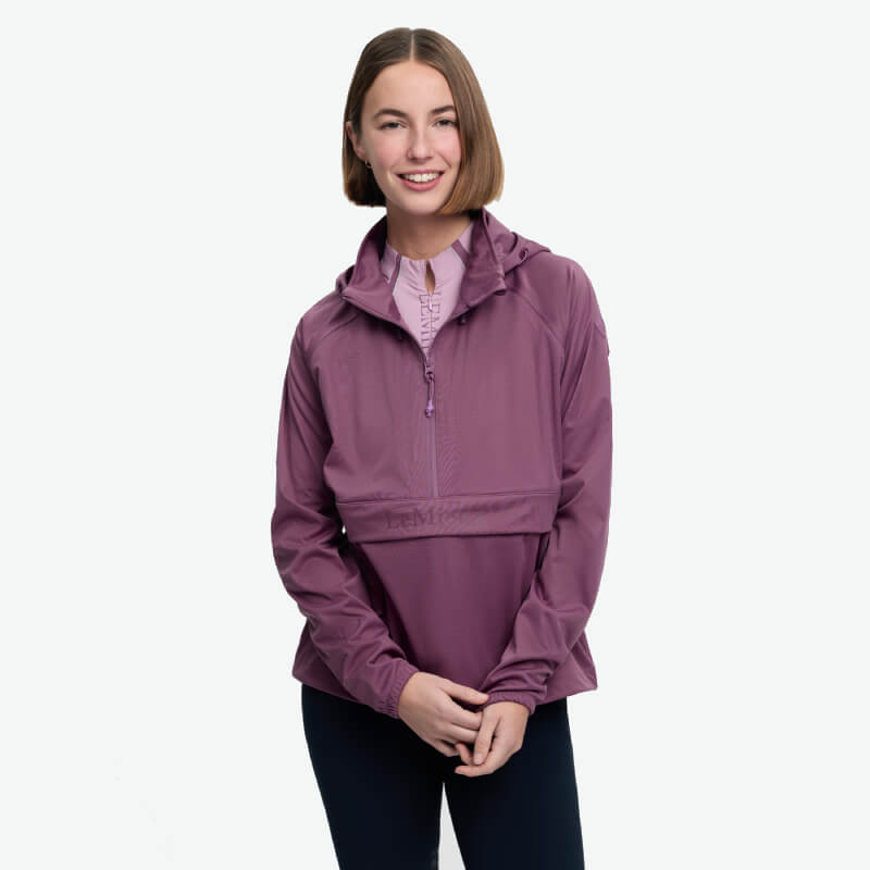 Smiling person in a LeMieux Perri Half Zip Waterproof Hoodie Mallow stands against white background.