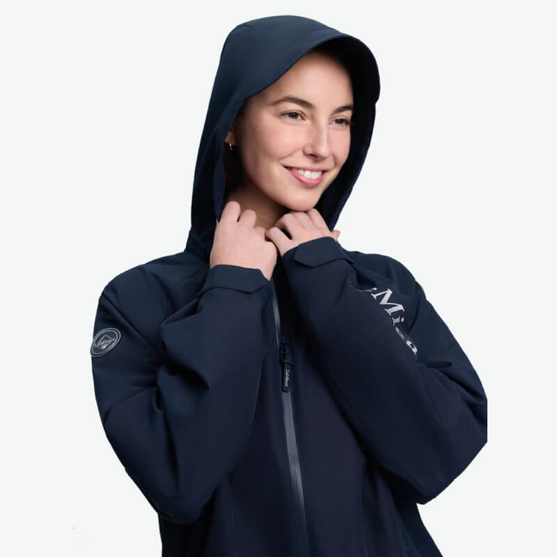 Smiling person in LeMieux Indra Waterproof Jacket Navy holding hood, on white background.