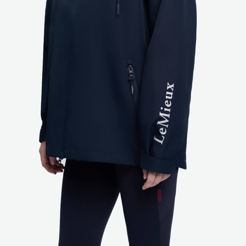 Person wearing a LeMieux Indra Waterproof Jacket Navy with text on the sleeve and black pants.