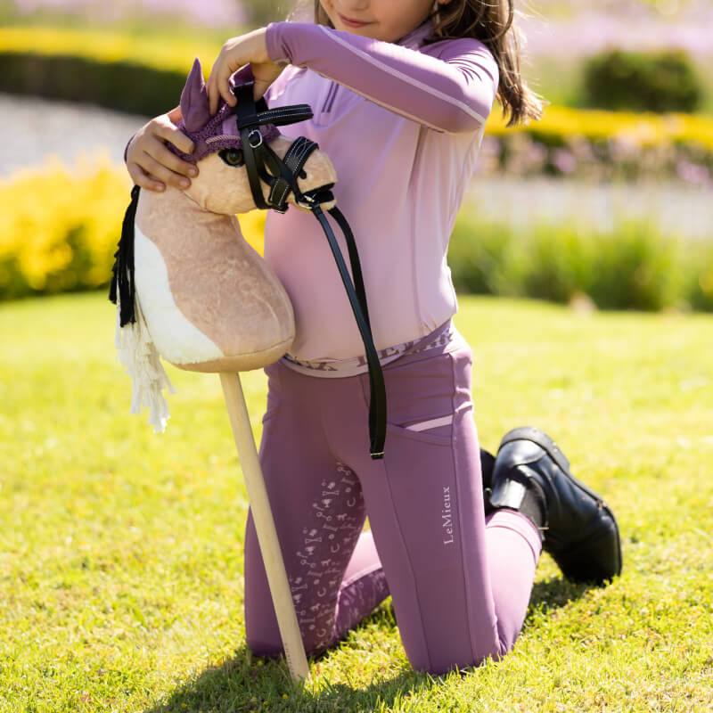 Child kneels on grass, adjusts bridle of LeMieux Hobby Horse Mini Toby.
