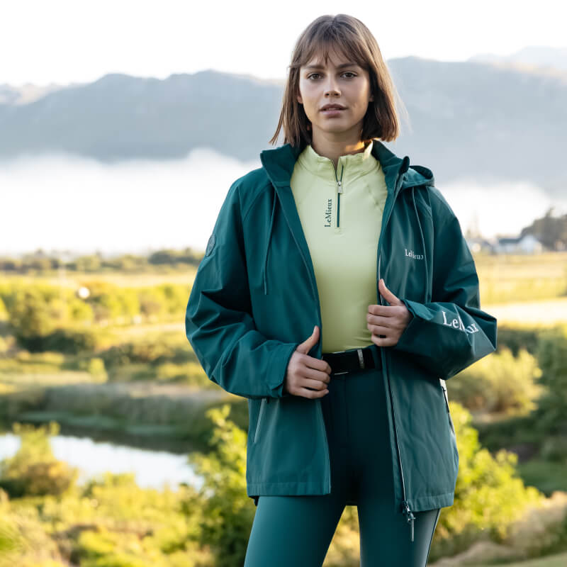 Woman in a LeMieux Indra Waterproof Jacket Jungle, smiling against a plain white background.