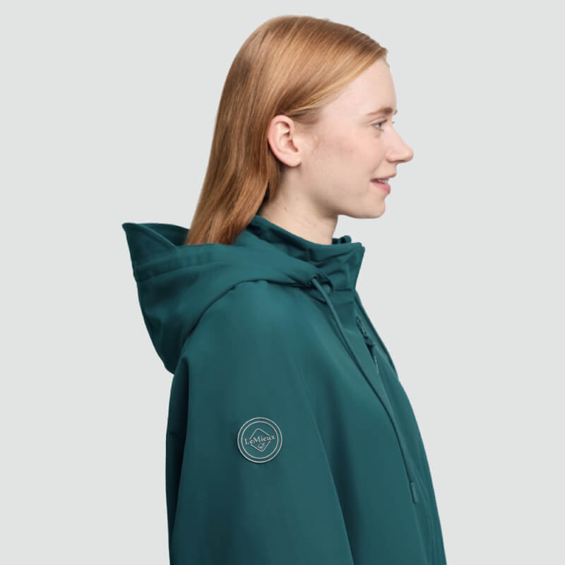 Person with light hair in LeMieux Indra Waterproof Jacket Jungle, facing right on plain background.