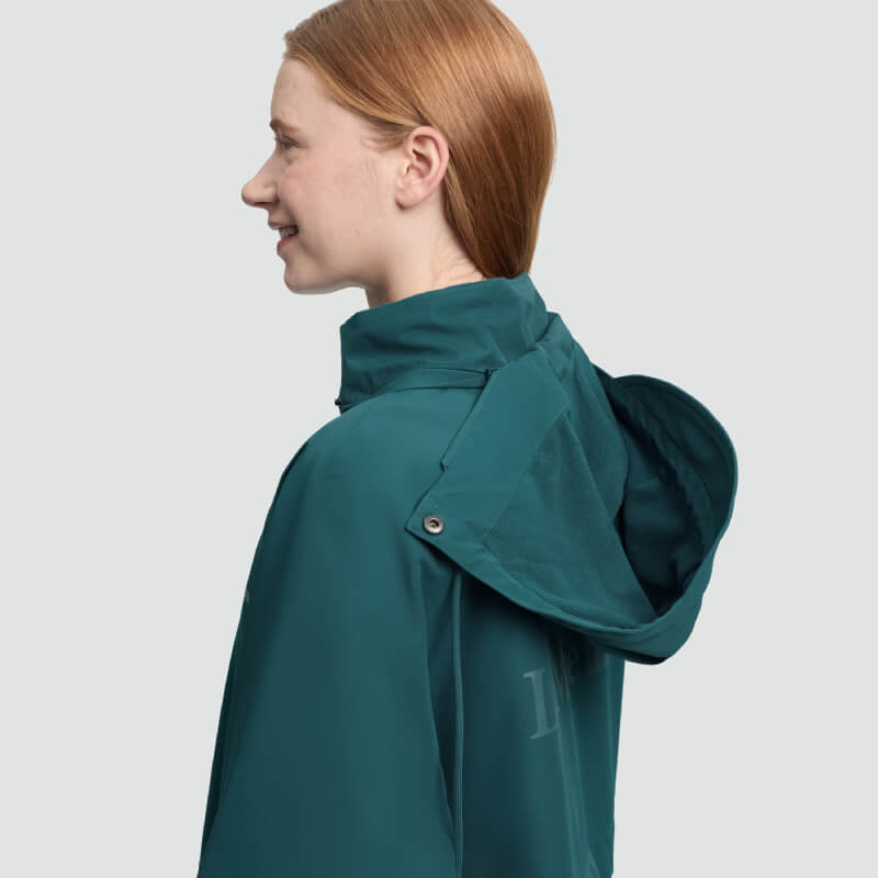 Long red-haired person in teal LeMieux Indra Waterproof Jacket Jungle, side view, smiling.
