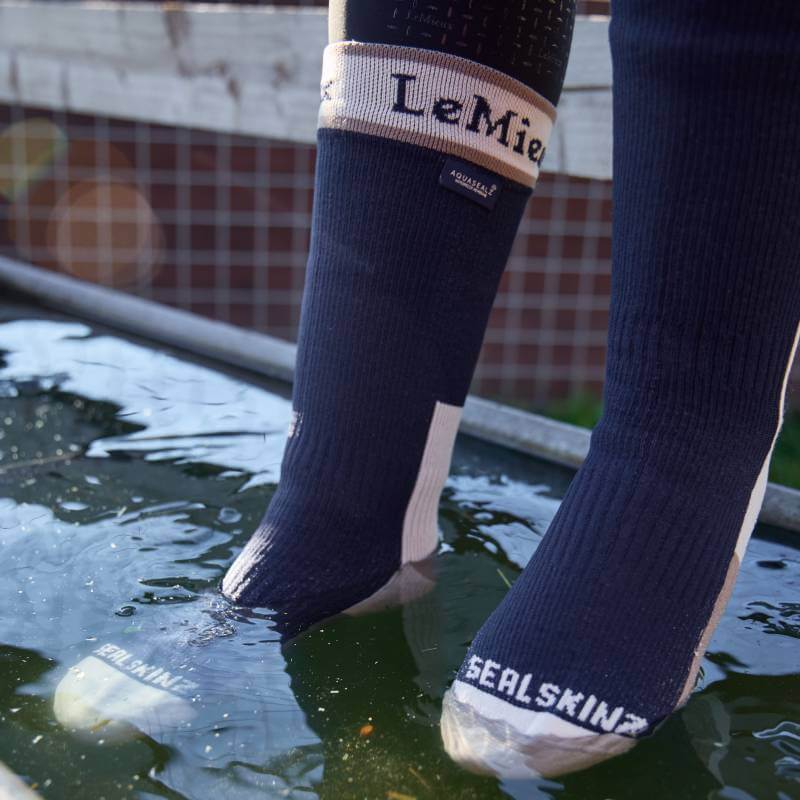 Person wears LeMieux x Sealskinz Waterproof Socks Navy, feet partially submerged in shallow water.