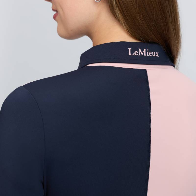 Woman in LeMieux Harlequin Rugby Shirt Baselayer Petal/Navy, logo on collar, back view.