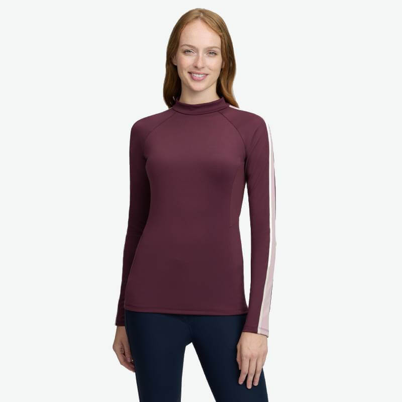 Woman wears LeMieux Talia Turtle Neck Baselayer Bramble, standing and smiling.