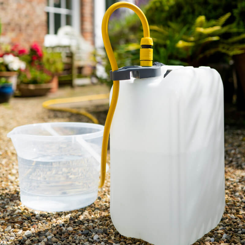 SealStop Valve in white plastic with a universal hose connector beside a clear bucket outdoors.