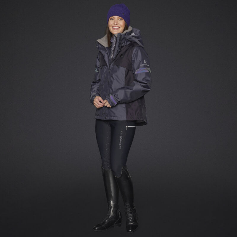 Smiling woman in a Mountain Horse Royal Grace Jacket in Deep Purple, beanie, and tall black boots.