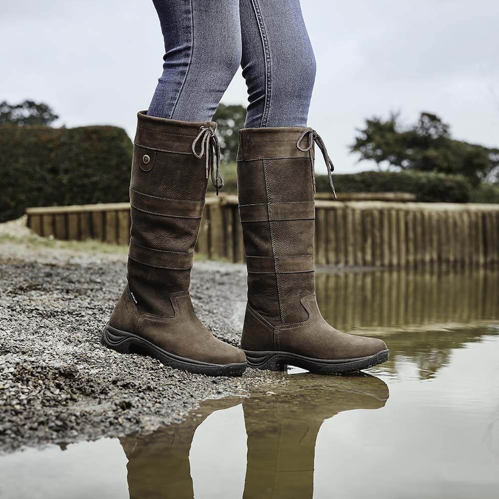 Wearing Dublin River Boots III and jeans, a person stands by a water puddle outdoors.