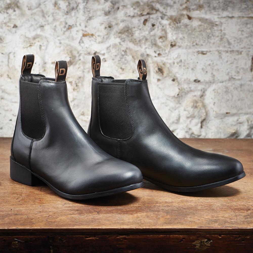 Dublin Foundation Childs Jodhpur Boots rest on wood with a light stone wall in the background.