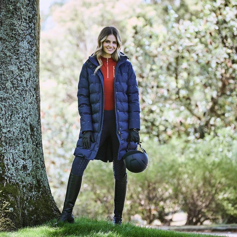 Smiling woman in Weatherbeeta Helsinki Heat Seal Quilted Jacket Navy Iris holds a black helmet.