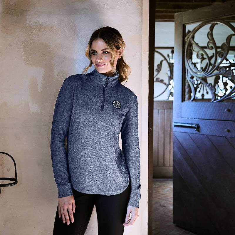 Woman wears a Weatherbeeta London Layer Long Sleeve Top Navy Iris indoors by an open wooden door.