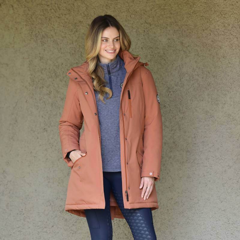 Woman in a Weatherbeeta Kyla II Waterproof Jacket Redwood Ladies by a textured beige wall.