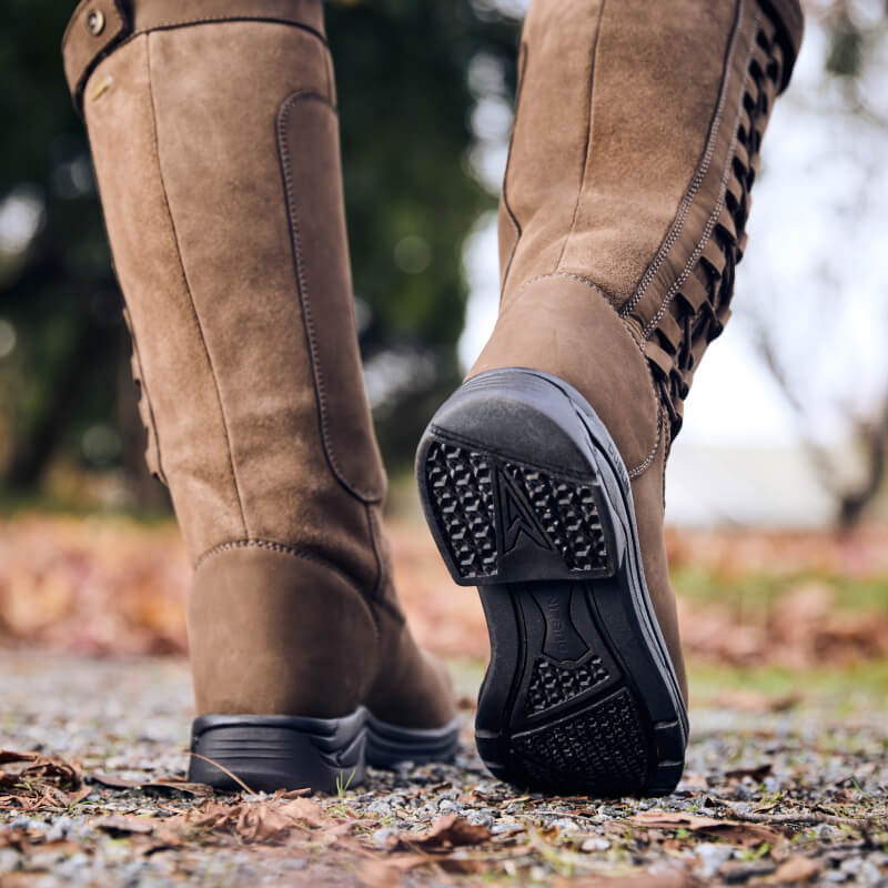 Close-up of a person wearing Dublin Pinnacle Boots III Chocolate by Dublin on a gravel path outdoors.
