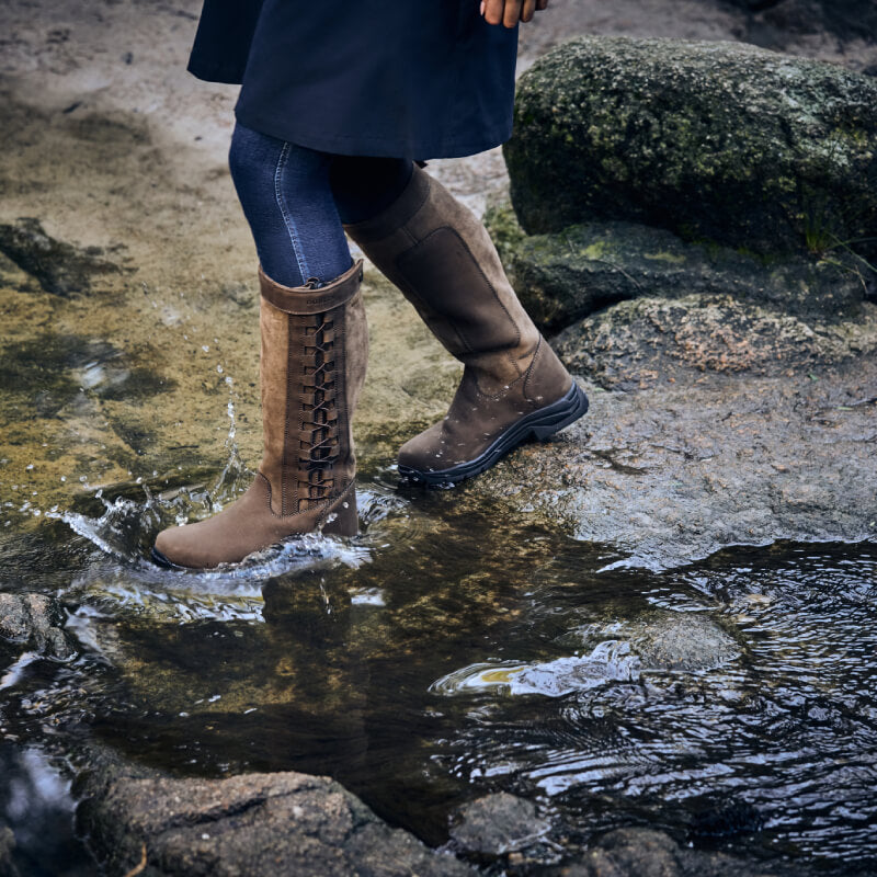 Wearing Dublin Pinnacle Boots III Chocolate, a person splashes through a shallow stream.