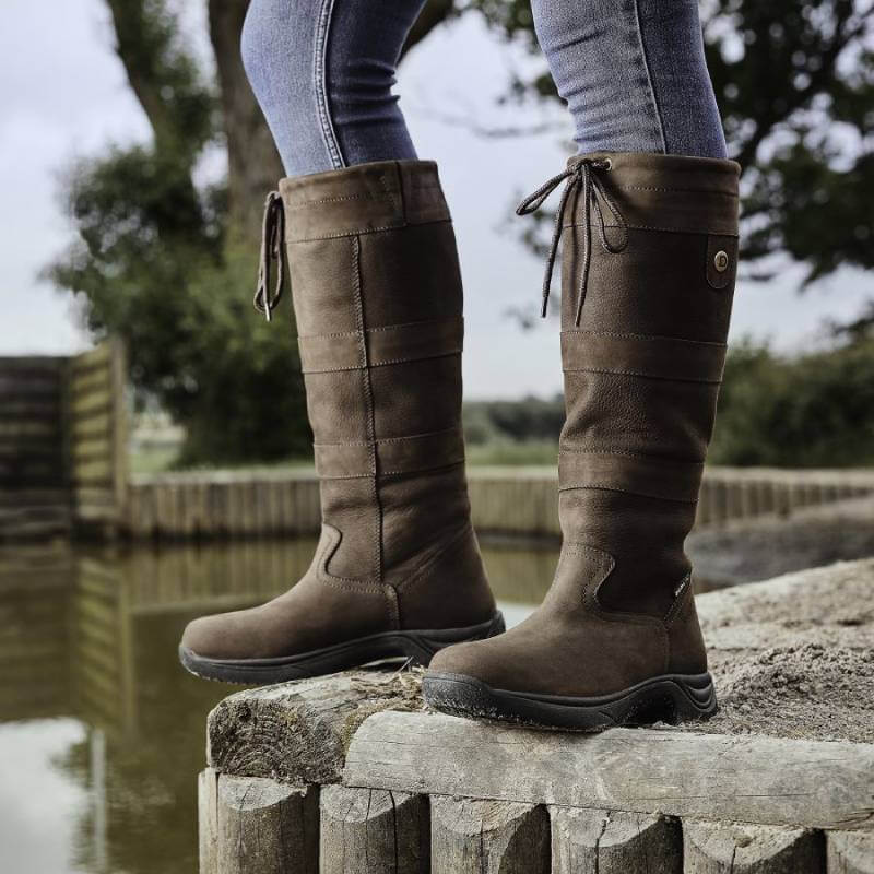 Person wearing Dublin River Boots III by Dublin stands near water on a wooden dock outdoors.