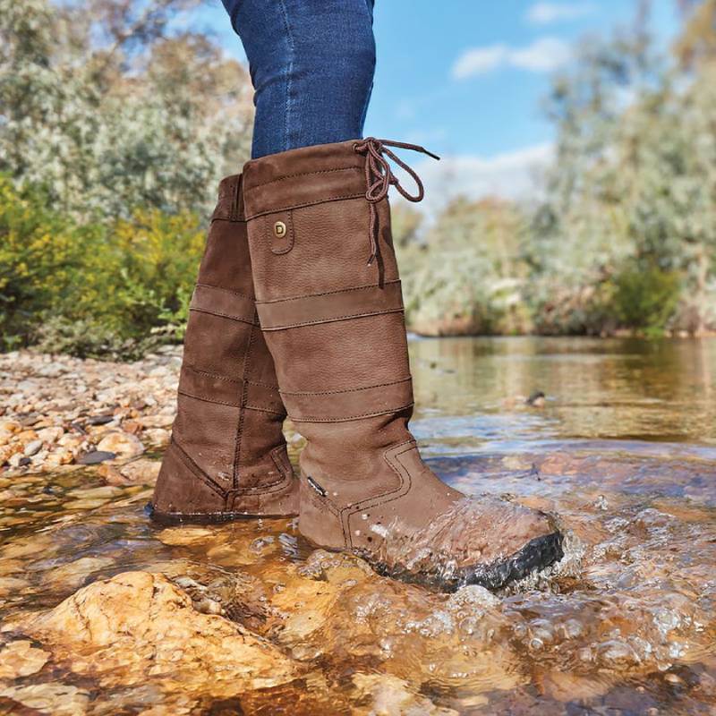 Wearing Dublin River Boots III, a person stands in a creek with water splashing around.