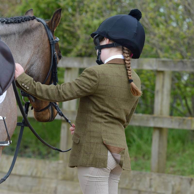 Girl in a Dublin Albany Tweed Child's Jacket stands by a horse, holding the reins.