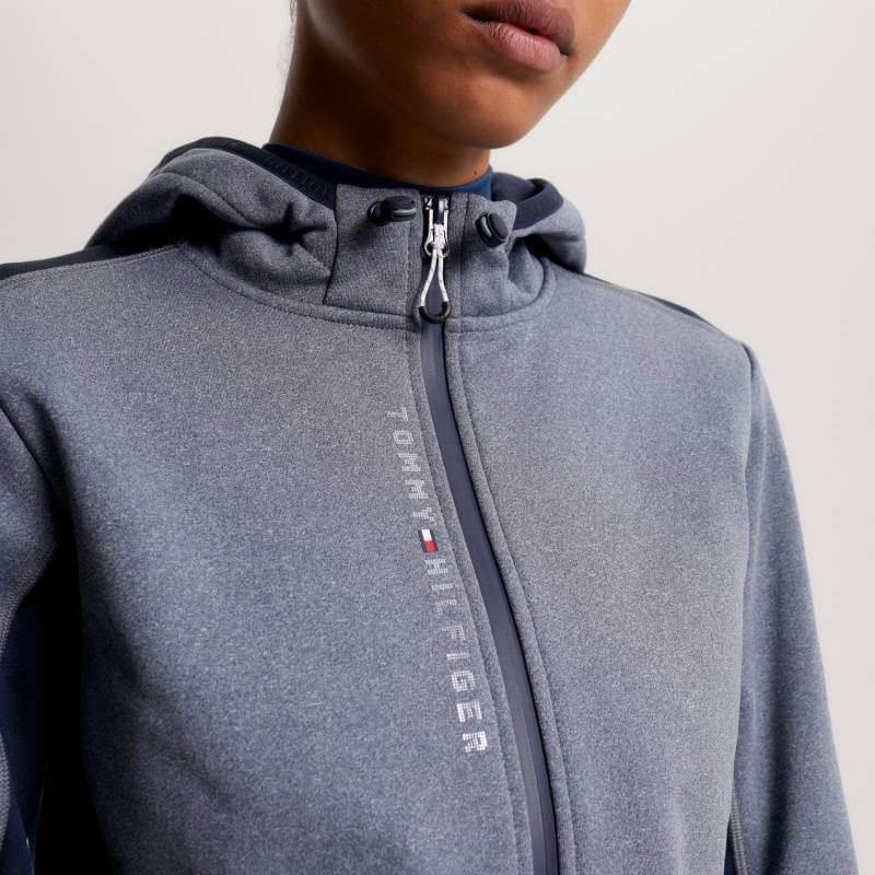 Person in a gray Tommy Hilfiger London Softshell Jacket with zip, hood, and front logo.