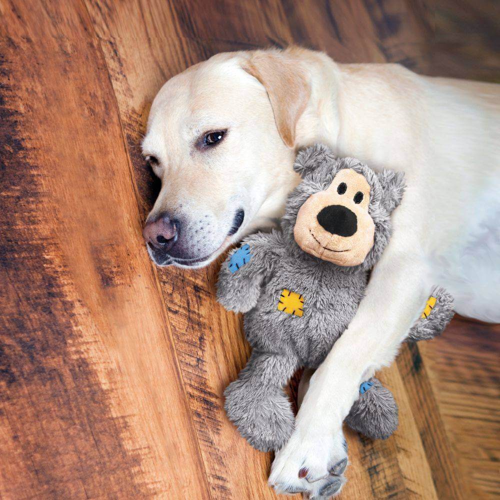 A yellow lab cuddles a durable Kong Wild Knots Bear dog toy on the floor.