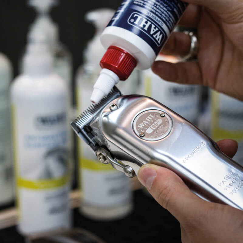 Applying Wahl Clipper Oil 118.3ml to silver Wahl blades with bottles in the background.