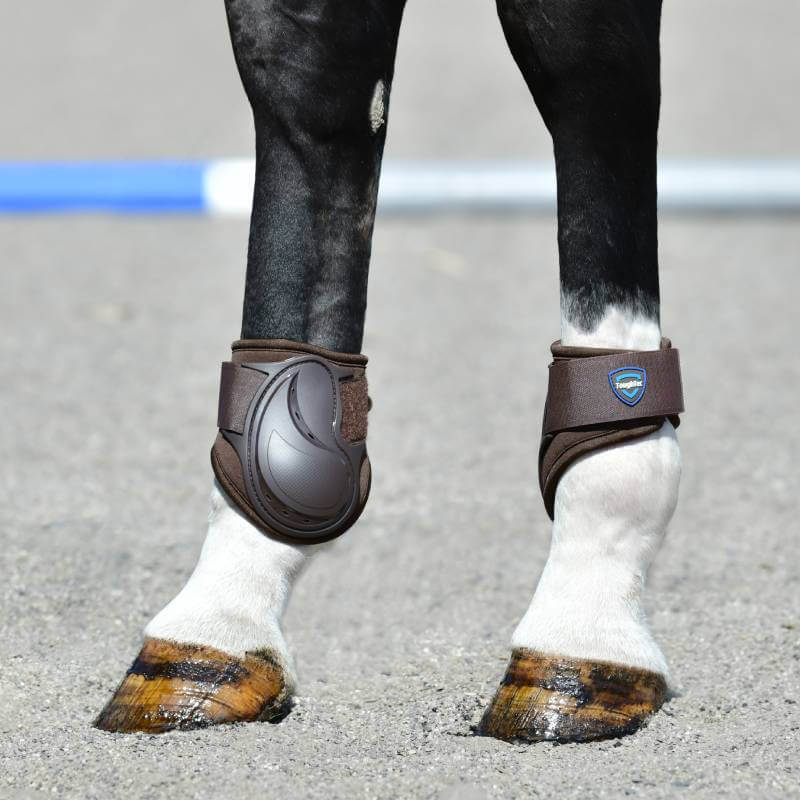 Close-up of Weatherbeeta Tough-Tec Essential Fetlock Boots Brown on horse's legs standing on gravel.