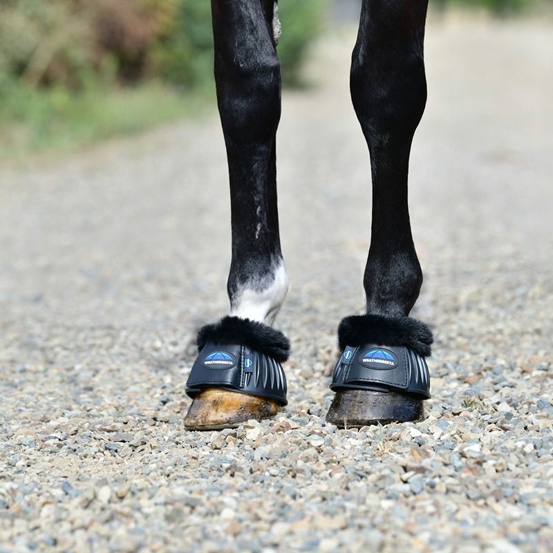 Weatherbeeta Tough-Tec Prime Fleece Trim Bell Boots on horse legs, black, on gravel path.