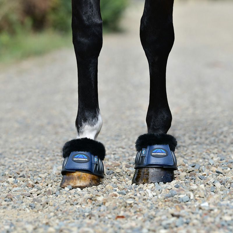 Weatherbeeta Tough-Tec Prime Fleece Trim Rubber Bell Boots protect a horse on a gravel path.