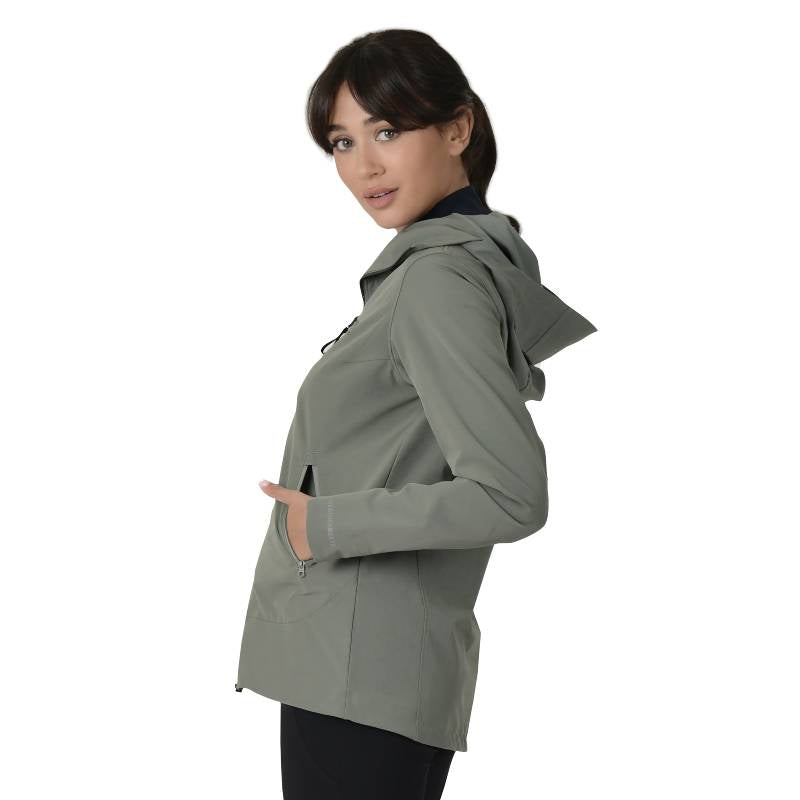 Woman in an olive Weatherbeeta stretch riding jacket, standing sideways with hands in pockets.