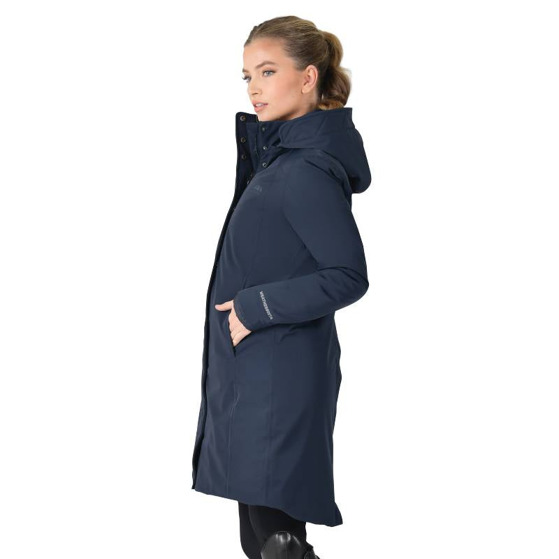 Woman wears Weatherbeeta All Purpose Waterproof Longline Equestrian Jacket Navy, hands in pockets.