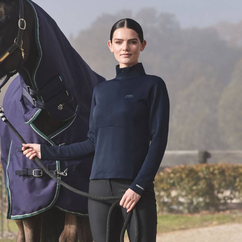 Woman wears Weatherbeeta Copper 1/2 Zip Top, holding horse in matching navy Weatherbeeta blanket.