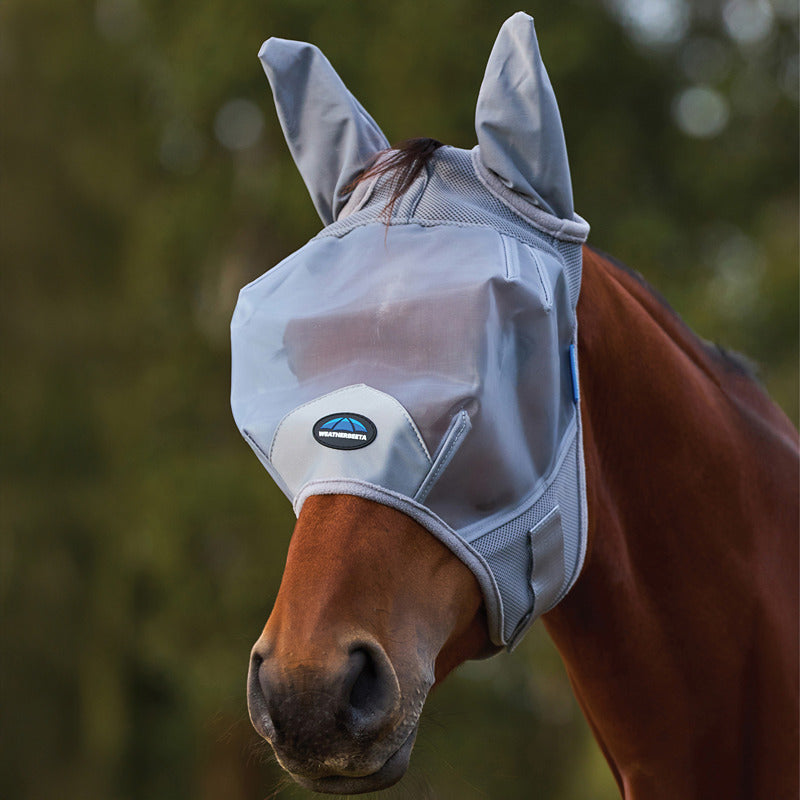 A horse outdoors wears a Weatherbeeta Comfitec Fine Mesh Fly Mask With Ears in grey.