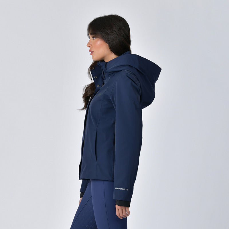Woman in Weatherbeeta Protect Waterproof Riding Jacket Navy standing sideways against plain background.