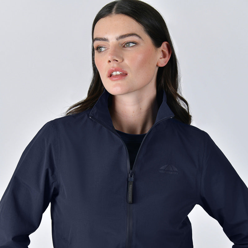 Woman with long dark hair wearing the Weatherbeeta Waterproof Team Jacket in navy, looking sideways.
