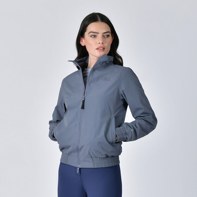 Woman in a Weatherbeeta Waterproof Team Jacket Slate Blue and navy pants against a light background.