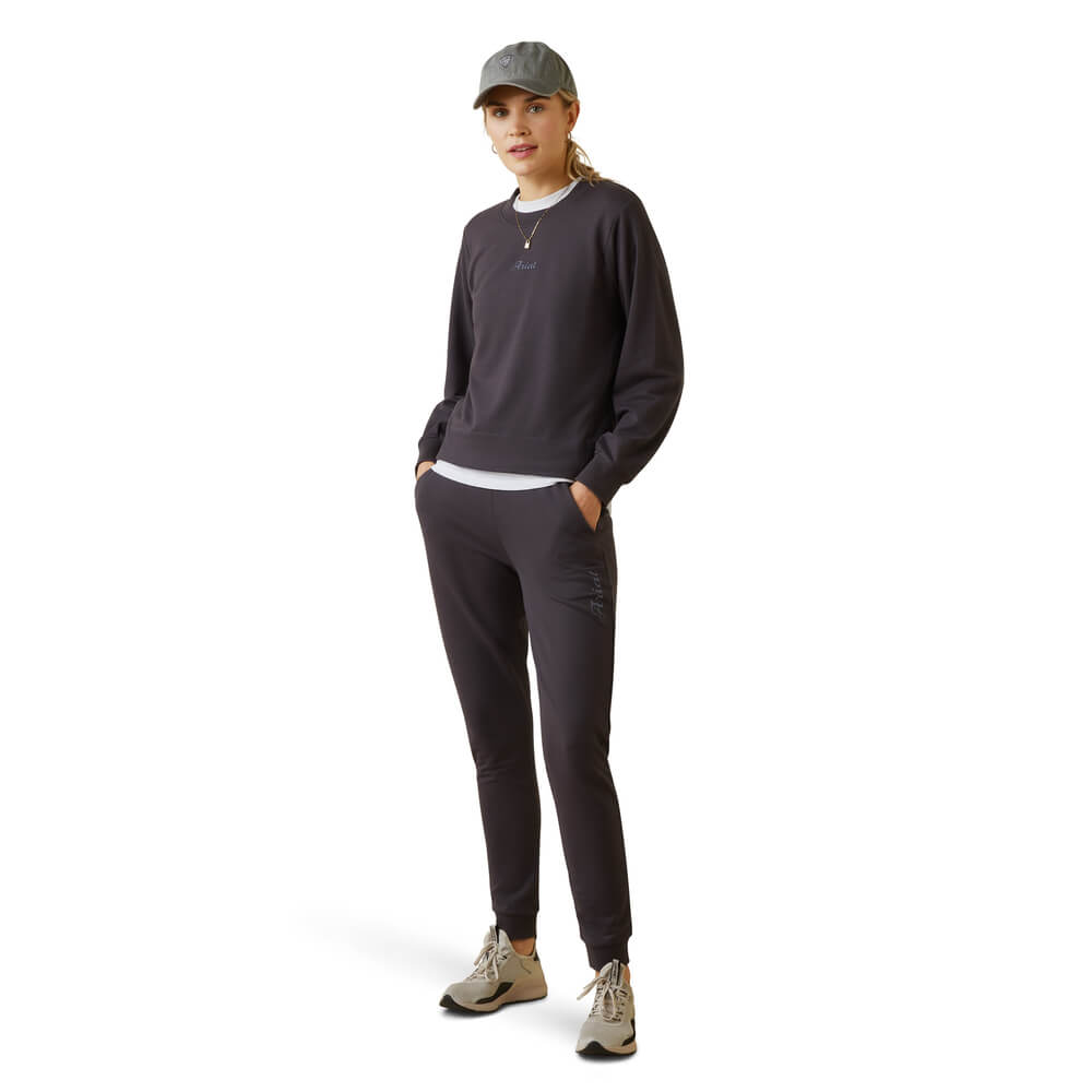 Woman wears the Ariat Memento Sweatshirt in Periscope, gray cap, and sneakers with hands in pockets.