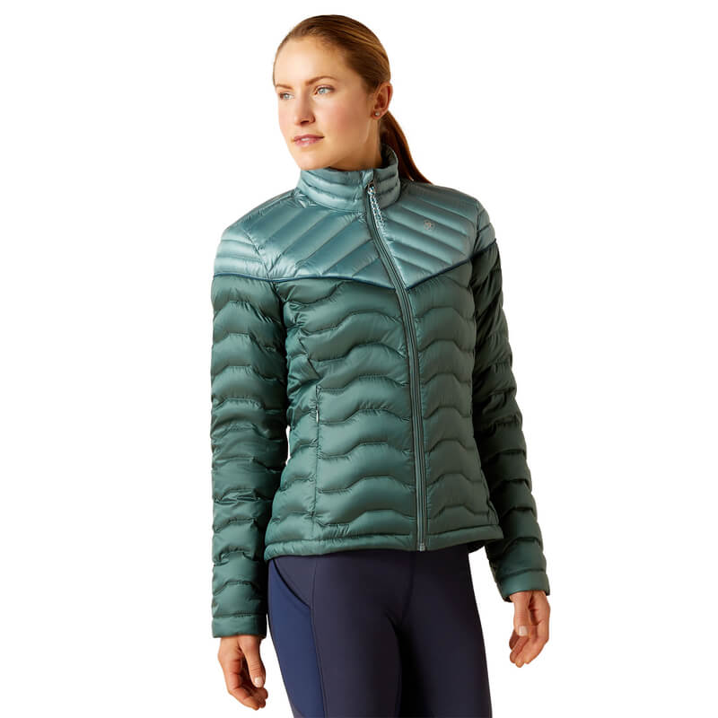 Woman in an Ariat Ideal Down Jacket Iridescent Arctic, navy leggings, looking left.