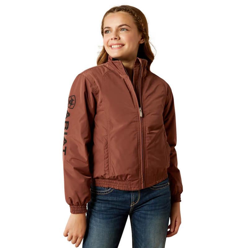 Girl in an Ariat Youth Stable Jacket Marron and jeans, smiling against a white background.