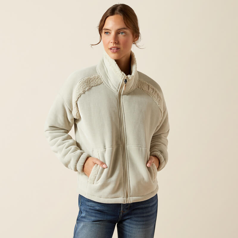 Woman wearing Ariat Womens Lafayette Full Zip Fleece Pelican with hands in pockets, plain background.