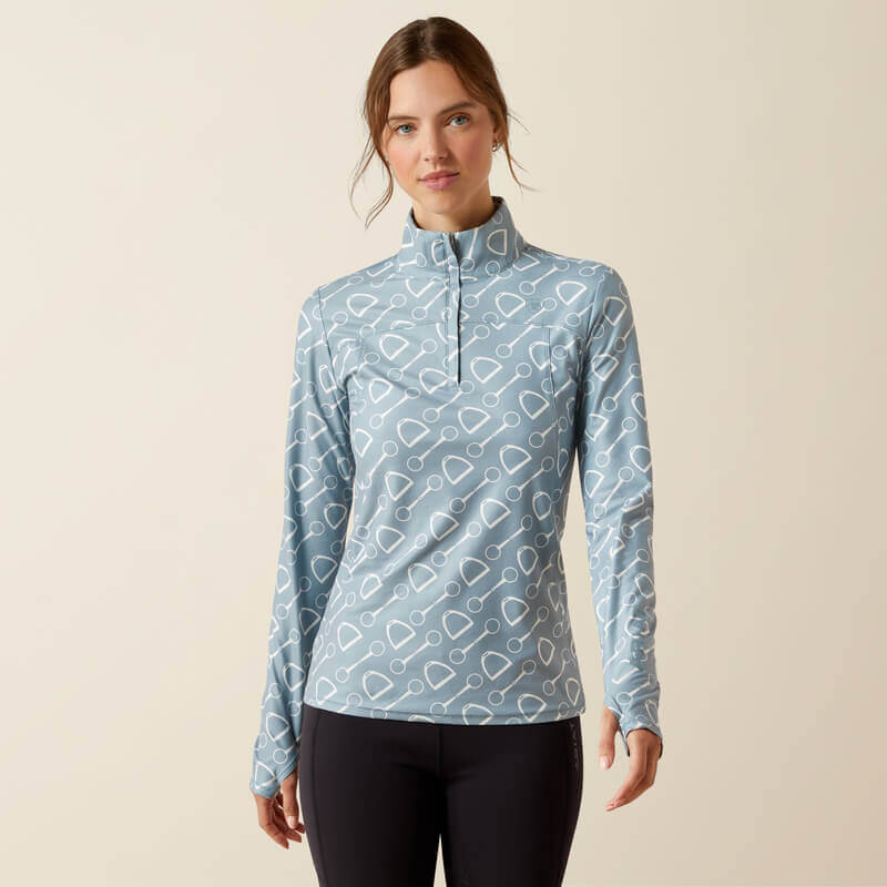 Woman in Ariat Womens Lowell 3.0 1/4 Zip Baselayer Hardware Print, blue top, black pants.