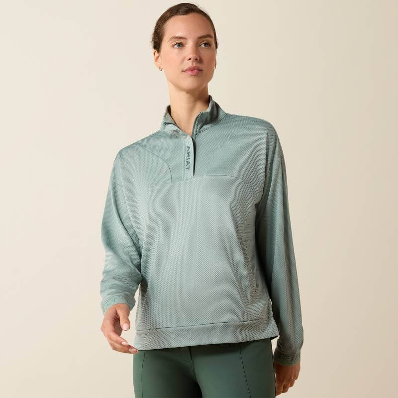 Woman in Ariat Breathe 1/2 Zip Pullover, Chinois Green, stands against a beige background.
