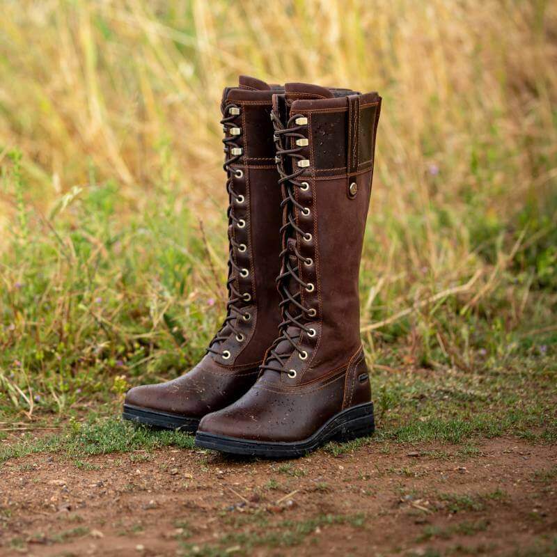 A pair of Ariat Womens Wythburn H2O Boots in Tobacco Brown stand on dirt.