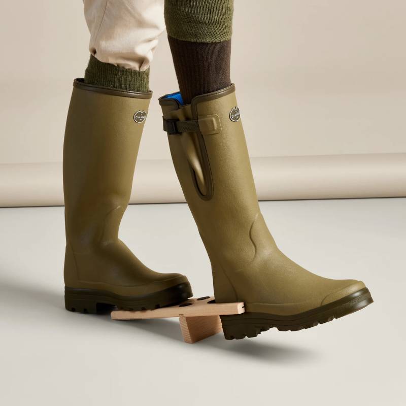 A person uses a Le Chameau Wooden Boot Jack Natural to remove a rubber boot.