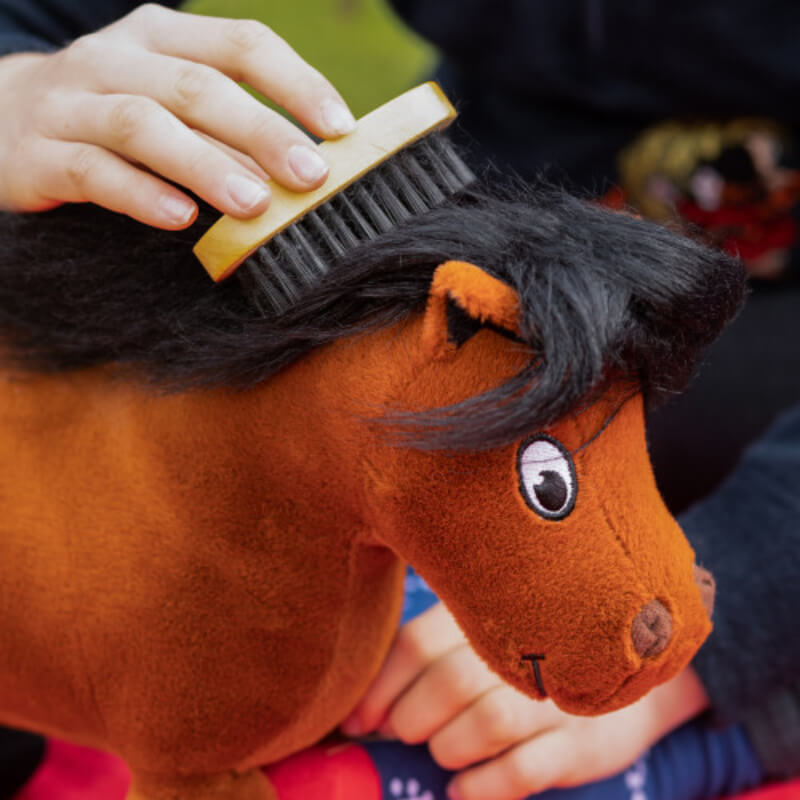 A hand brushes the mane of Thelwell Ponies Fiona & Merrylegs plush with a black brush.