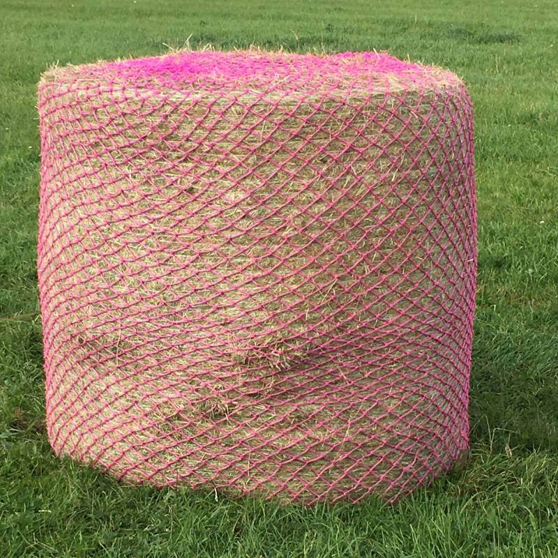 An Elico Wild Boar Bale Net Large Pink covers a round hay bale on green grass.