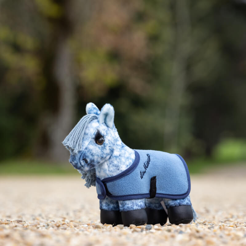 LeMieux Tiny Pony Sam, a blue plush pony, stands outdoors on a gravel path.
