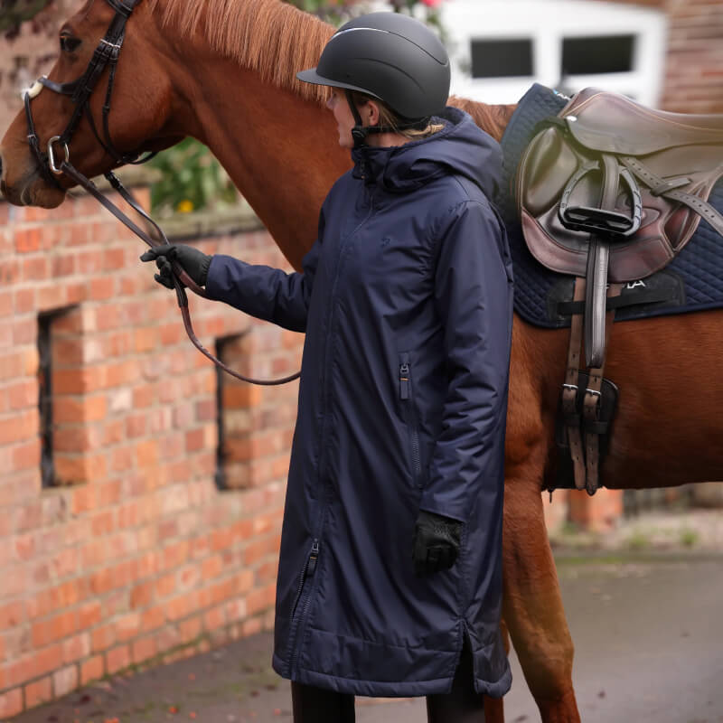 Person in an Aubrion Core All Weather Robe Unisex YR Navy holds a brown horse by the reins.